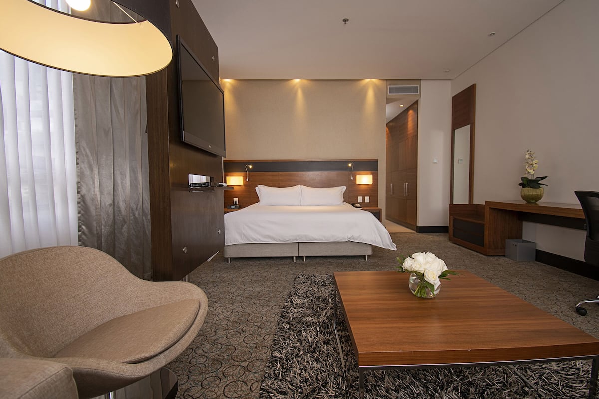 Hotelkamer met een bed, een bureau, een stoel, een televisie en een vaas met bloemen.