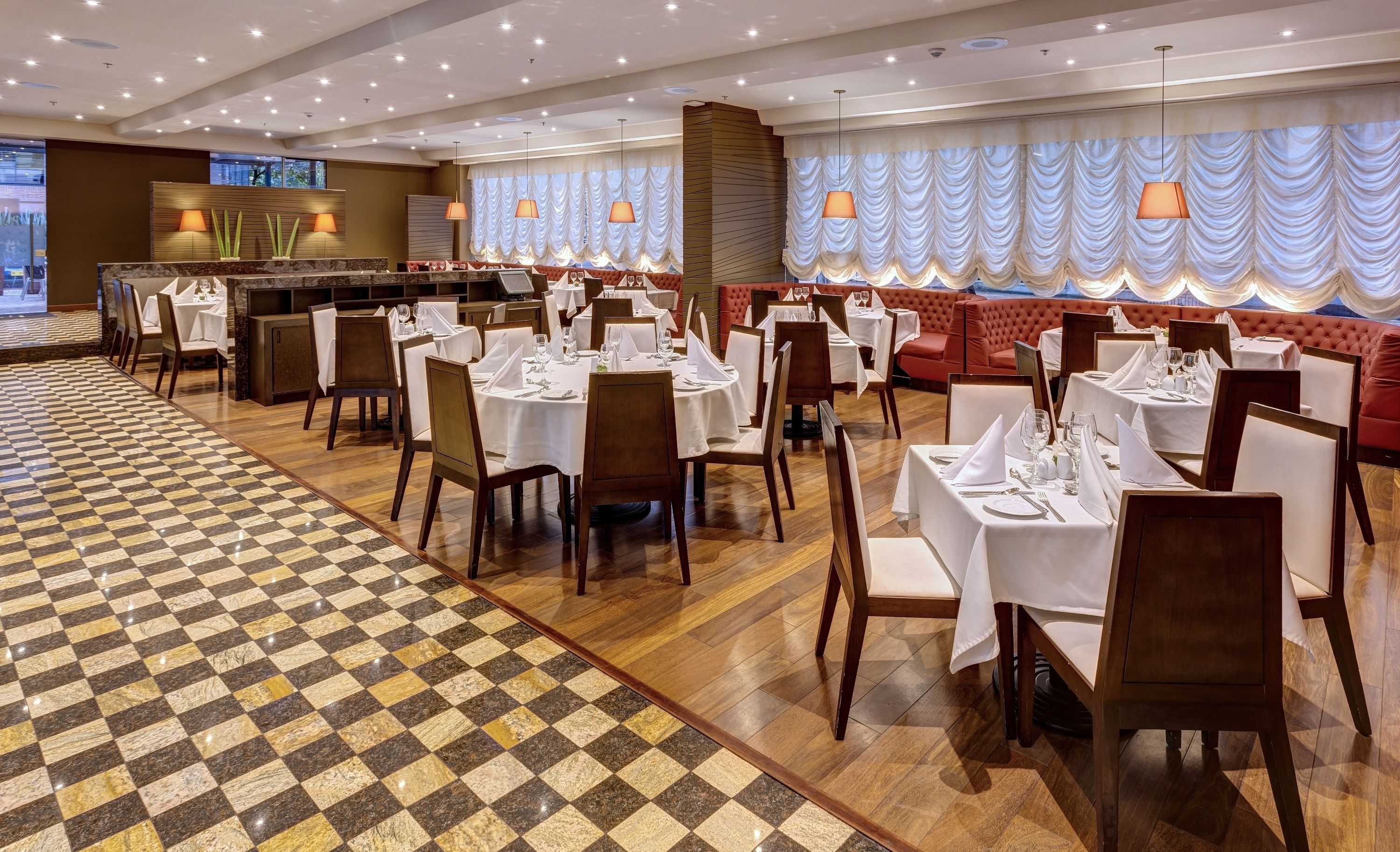 A restaurant with round tables set for dining, a checkered floor pattern, and a red upholstered booth area.