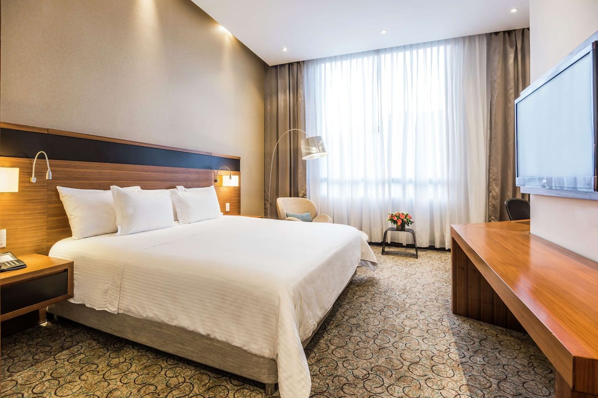 Een hotelkamer met een groot bed, een bureau, een stoel, een lamp en een televisie.