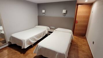 A room with two single beds, a small table, and a wall-mounted light fixture.