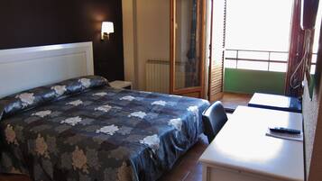 Habitación de hotel con cama, escritorio, silla, ventana y puerta que da a un balcón.