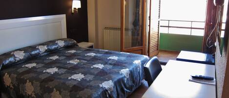 A hotel room with a bed, a desk, a chair, a window, and a door leading to a balcony.