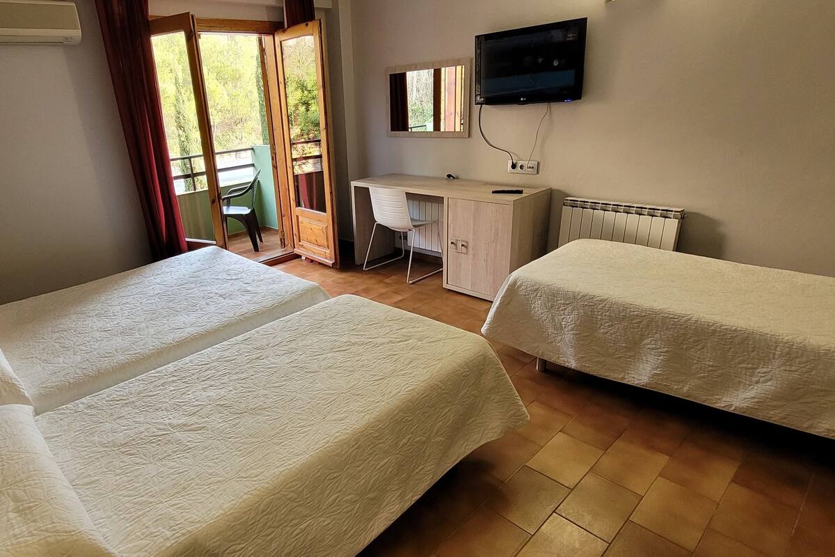 A room with two beds, a desk, a chair, a TV, and a window with curtains.