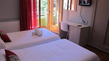 A hotel room with two beds, a desk, a TV, and a balcony with red curtains.