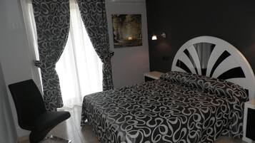 Un dormitorio con cama, una silla, una mesita de noche y una lámpara de pared.