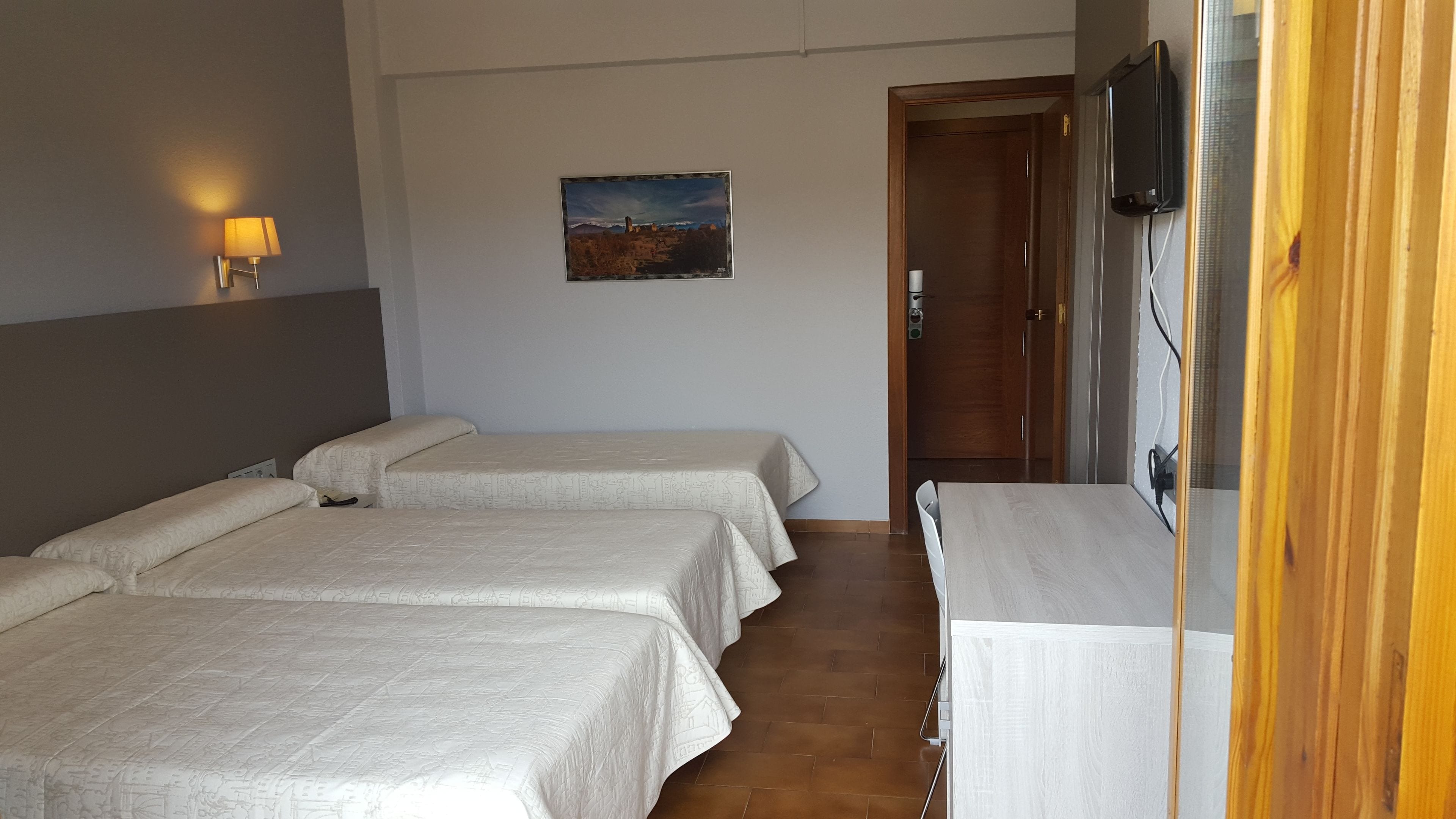 A hotel room with two beds, a painting on the wall, a TV mounted on the wall, and a wooden door.