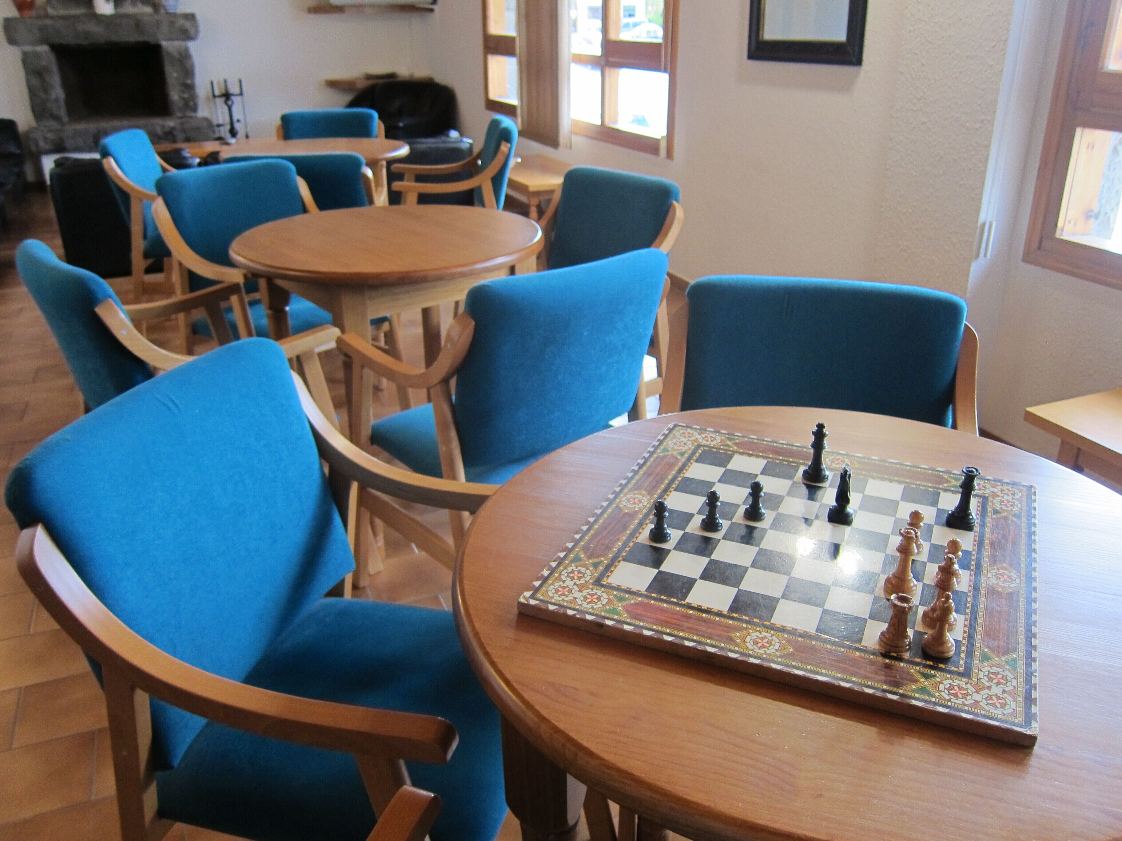 A room with a chessboard on a wooden table surrounded by blue chairs.