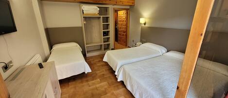 A bedroom with two single beds, a wooden wardrobe, a small desk with a telephone, and a wall-mounted TV.