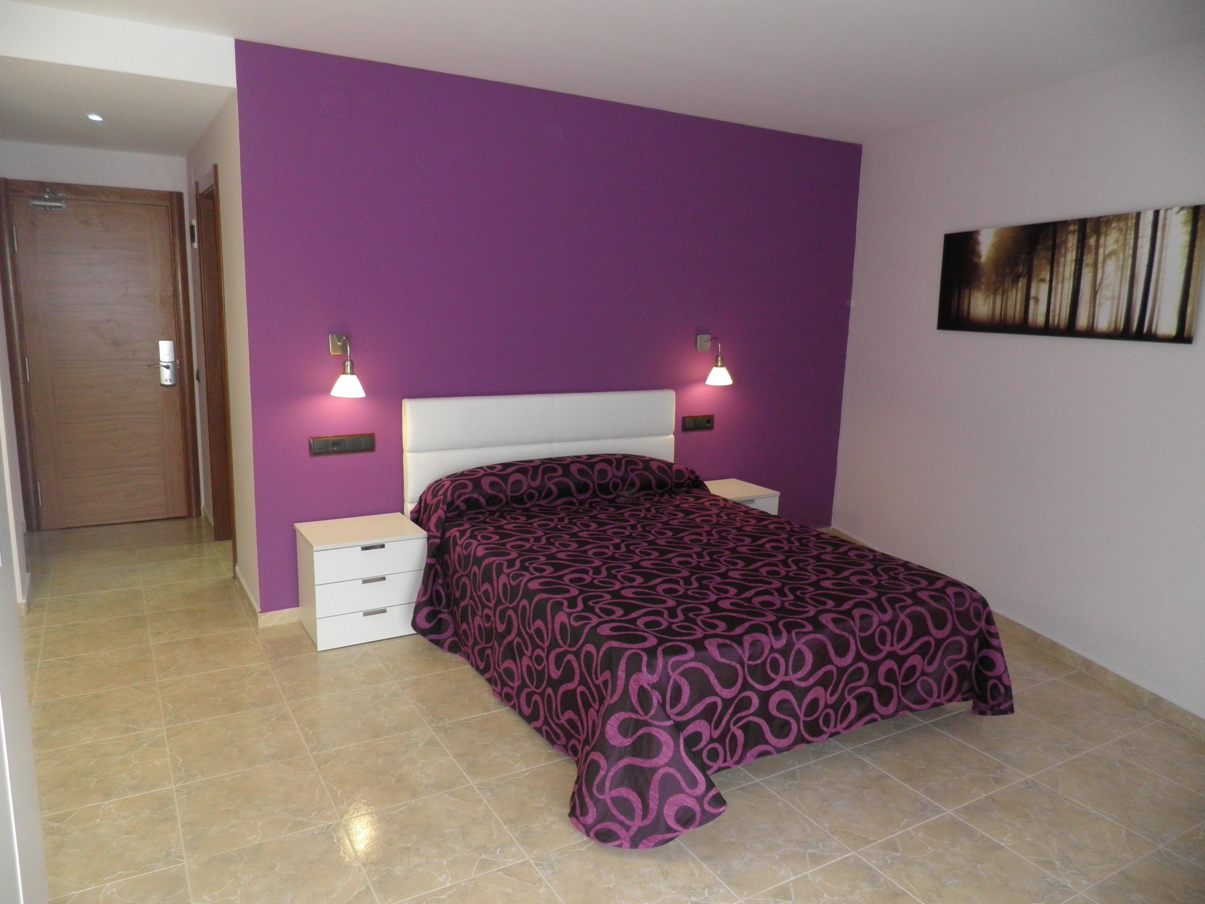 A bedroom with a purple wall, a white bed, two bedside tables with lamps, and a door.