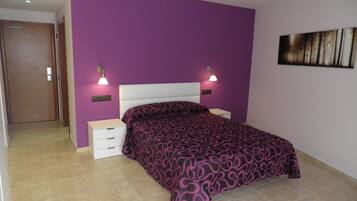 A bedroom with a purple wall, a white bed, two bedside tables with lamps, and a door.