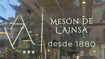 Ett fönster med texten ”MESÓN DE L’ÀINSA sedan 1880” och en geometrisk design.