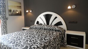 Un dormitorio moderno con un cabecero curvo original, ropa de cama estampada e iluminación montada en la pared.