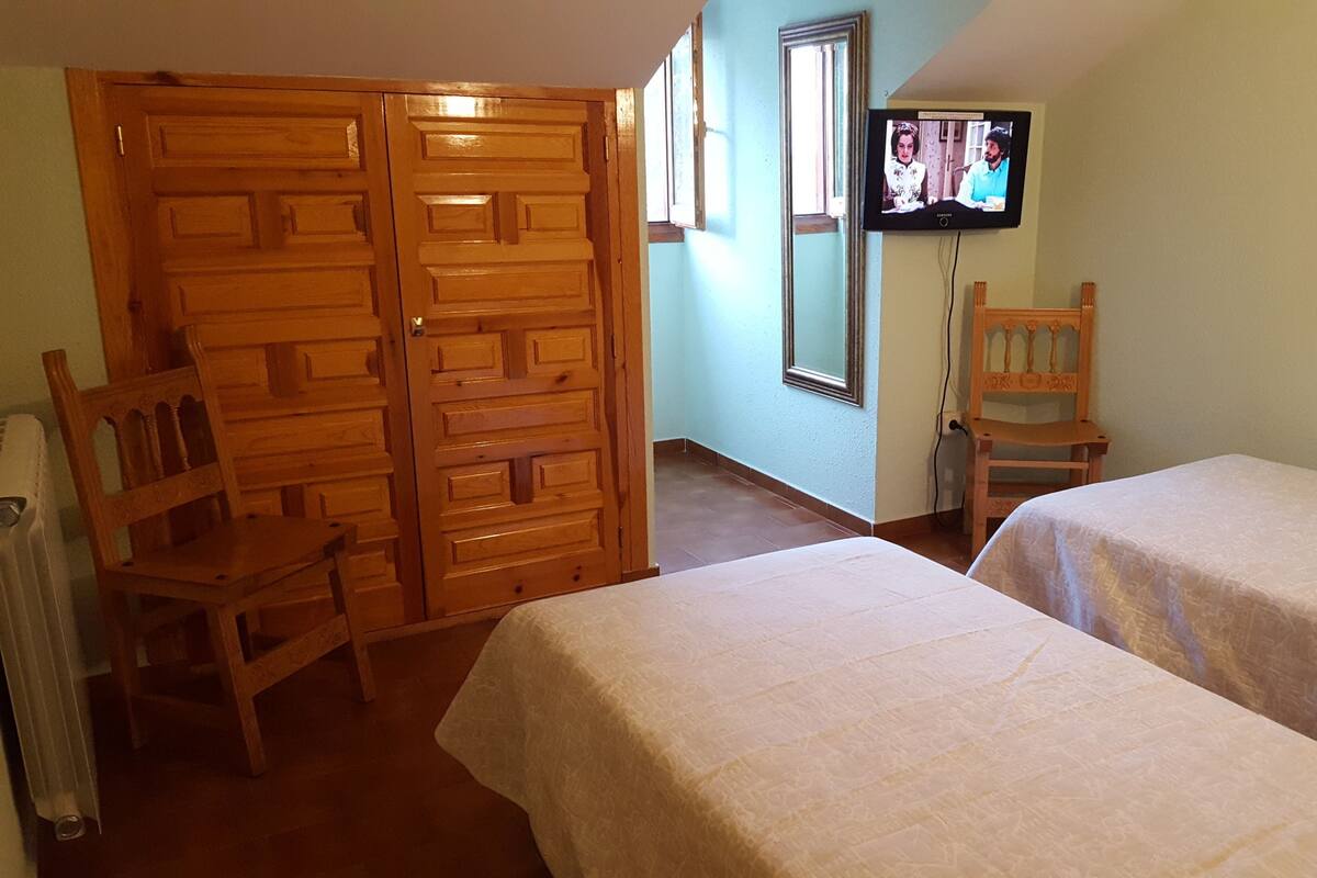 A room with two beds, a wooden wardrobe, a television, and a chair.