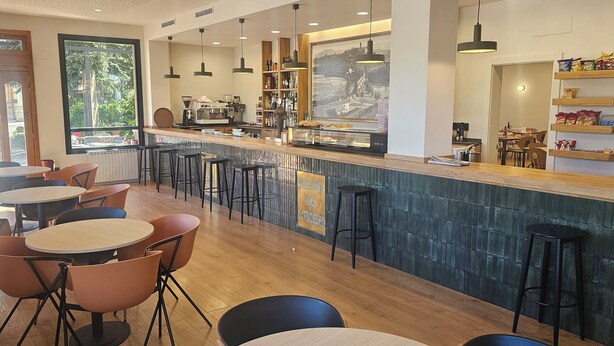 Un café moderno con zona de bar, asientos y vistas al exterior.