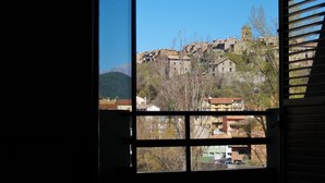 Vista a través de una ventana de un pueblo en una colina con edificios de piedra tradicionales y un cielo azul despejado.