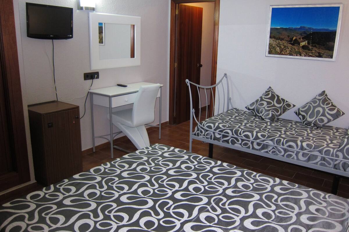 A bedroom with a bed, a desk, a chair, a TV, and a door.