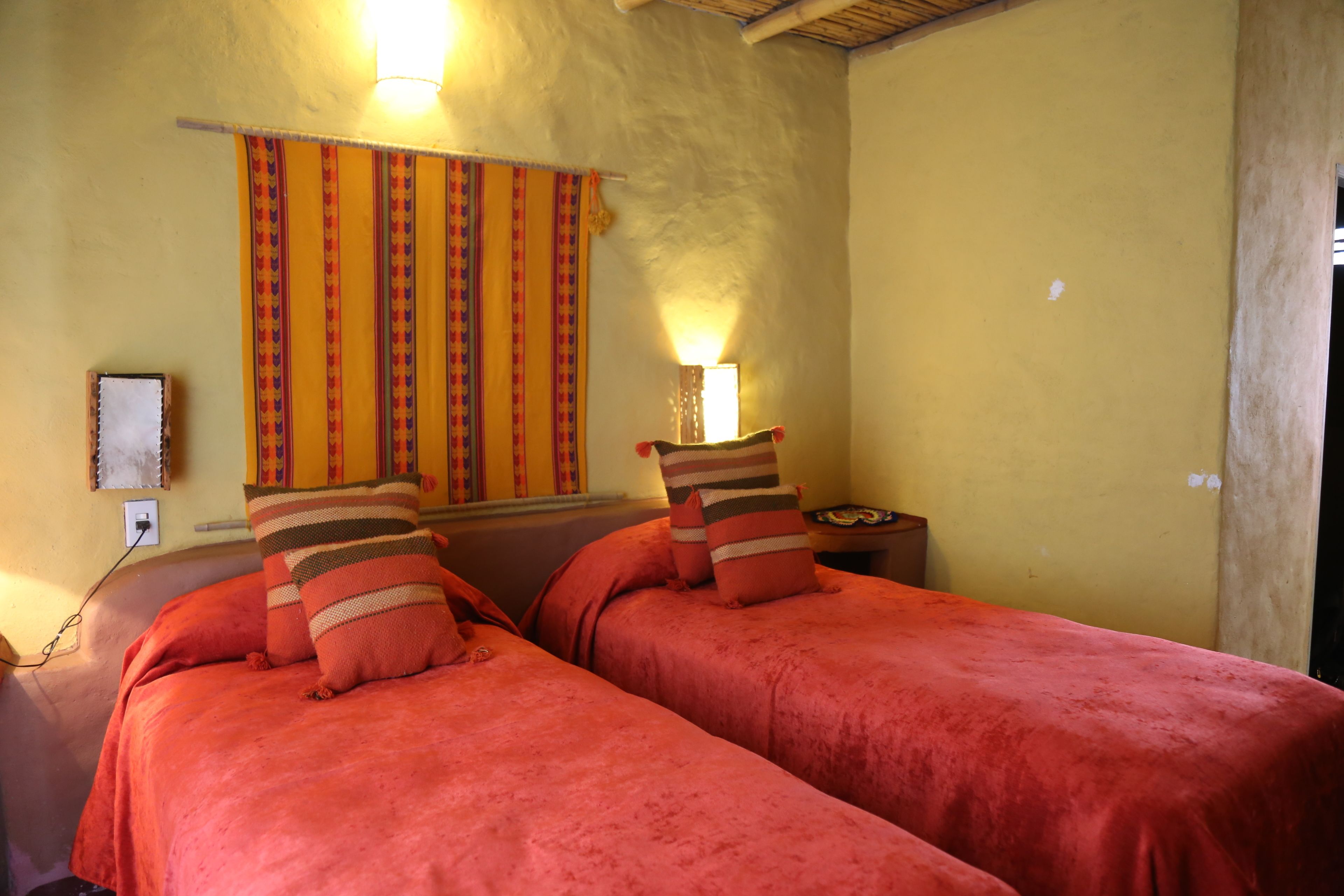 Una habitación con dos camas, una lámpara de pared y una cortina.