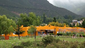 A yellow building with a thatched roof, surrounded by trees and a mountainous backdrop.