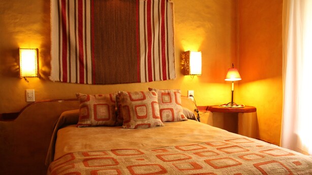 A neatly made bed with patterned pillows and a blanket, a striped wall hanging, and two wall-mounted lamps.