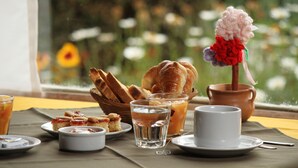A breakfast setting with croissants, pastries, and beverages on a table by a window with a view of flowers.
