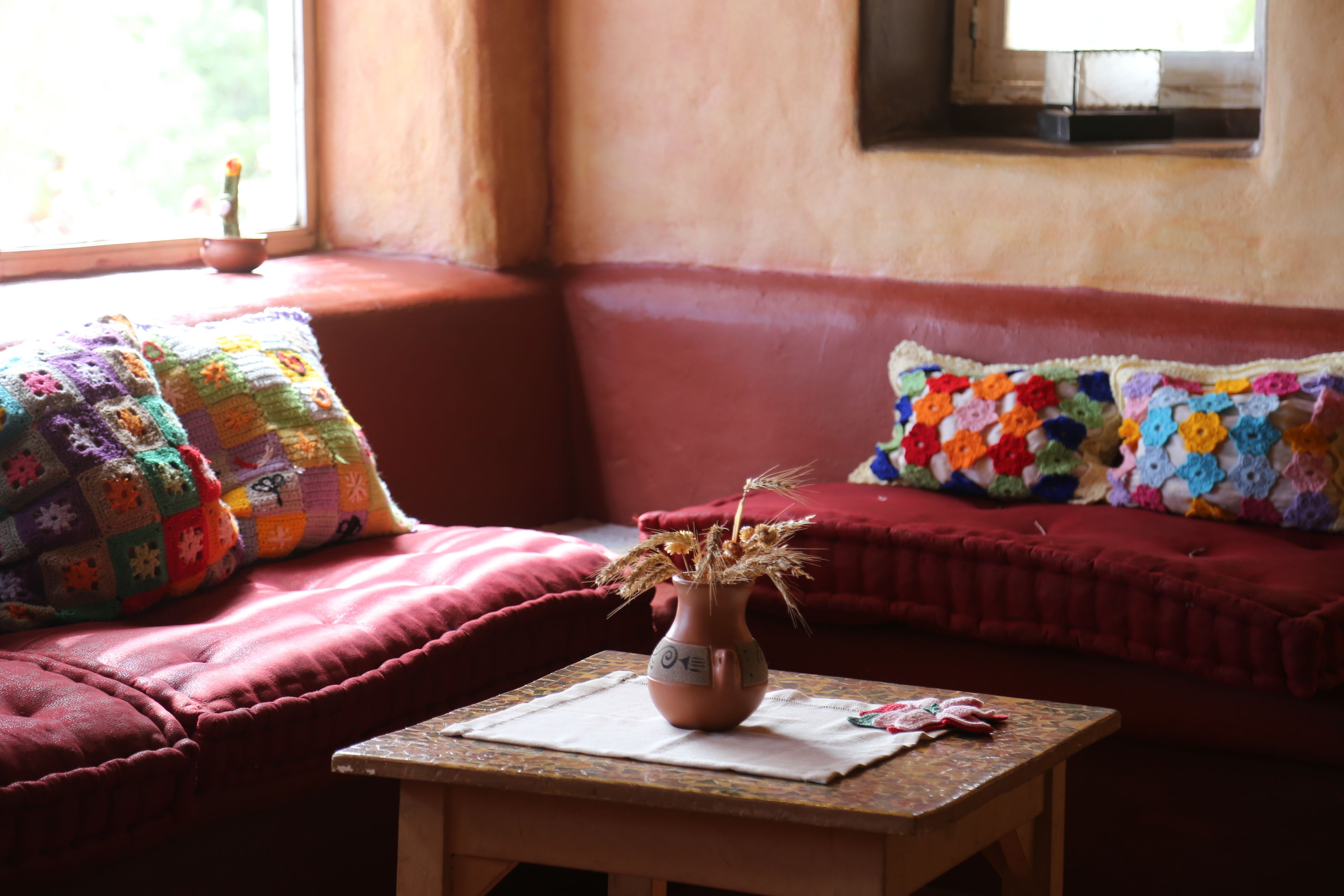A cozy living room with a red sofa, a small table with a vase, and colorful quilts on the cushions.
