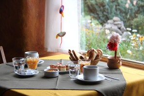 Desayuno preparado para dos personas, con platos, tazas y una cesta de pan.