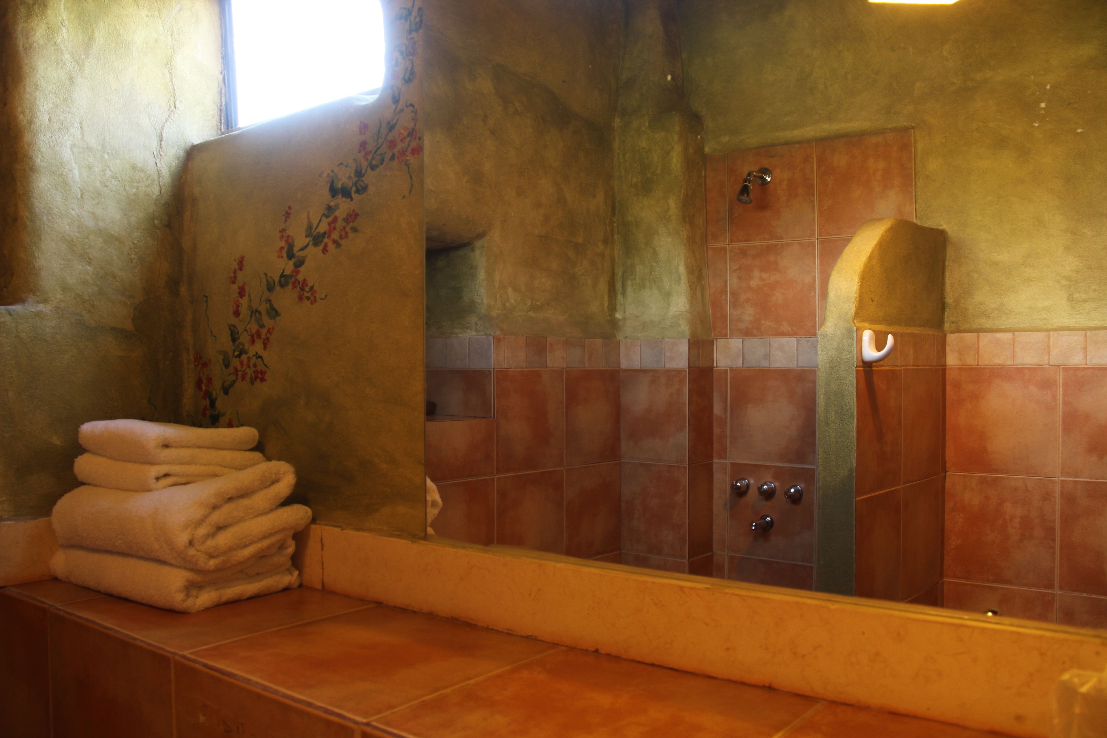 Een badkamer met een grote spiegel, een stapel handdoeken en een douche met een betegelde wand.