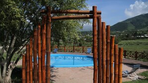 A bamboo archway leading to a swimming pool with a clear view of a mountainous landscape in the background.