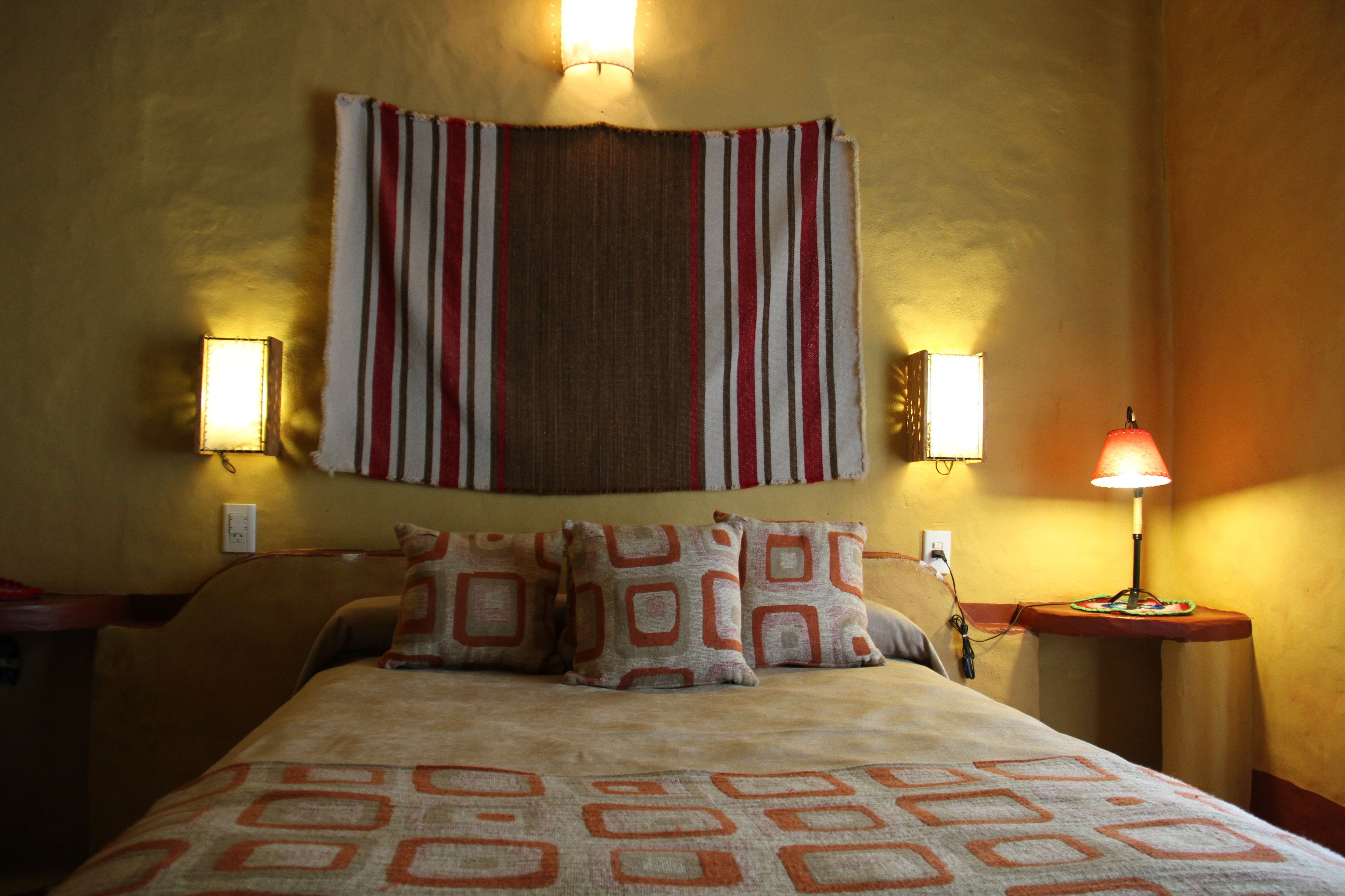 A neatly made bed with patterned pillows and a striped headboard. There are two wall-mounted lamps on either side of the bed.