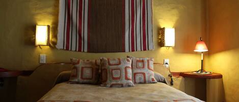 A neatly made bed with patterned pillows and a striped headboard. There are two wall-mounted lamps on either side of the bed.