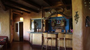 A cozy bar area with wooden beams, a bar counter, and two bar stools. - Posada La Guadalupe (Tafi del Valle)