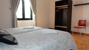 Een kamer met twee bedden, een kledingkast, een rode stoel en een raam met gordijnen.