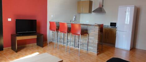 A compact kitchen with a TV, a small bar area with stools, a refrigerator, and a microwave.