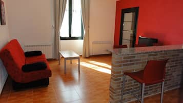 Quarto com sofá vermelho, mesa pequena, balcão de tijolos e cadeira vermelha.