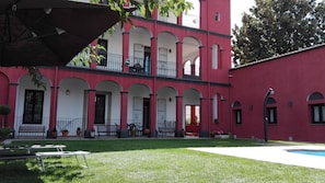 Ein zweistöckiges Gebäude mit roter Fassade, mehreren Balkonen und einem kleinen Innenhof mit Pool.