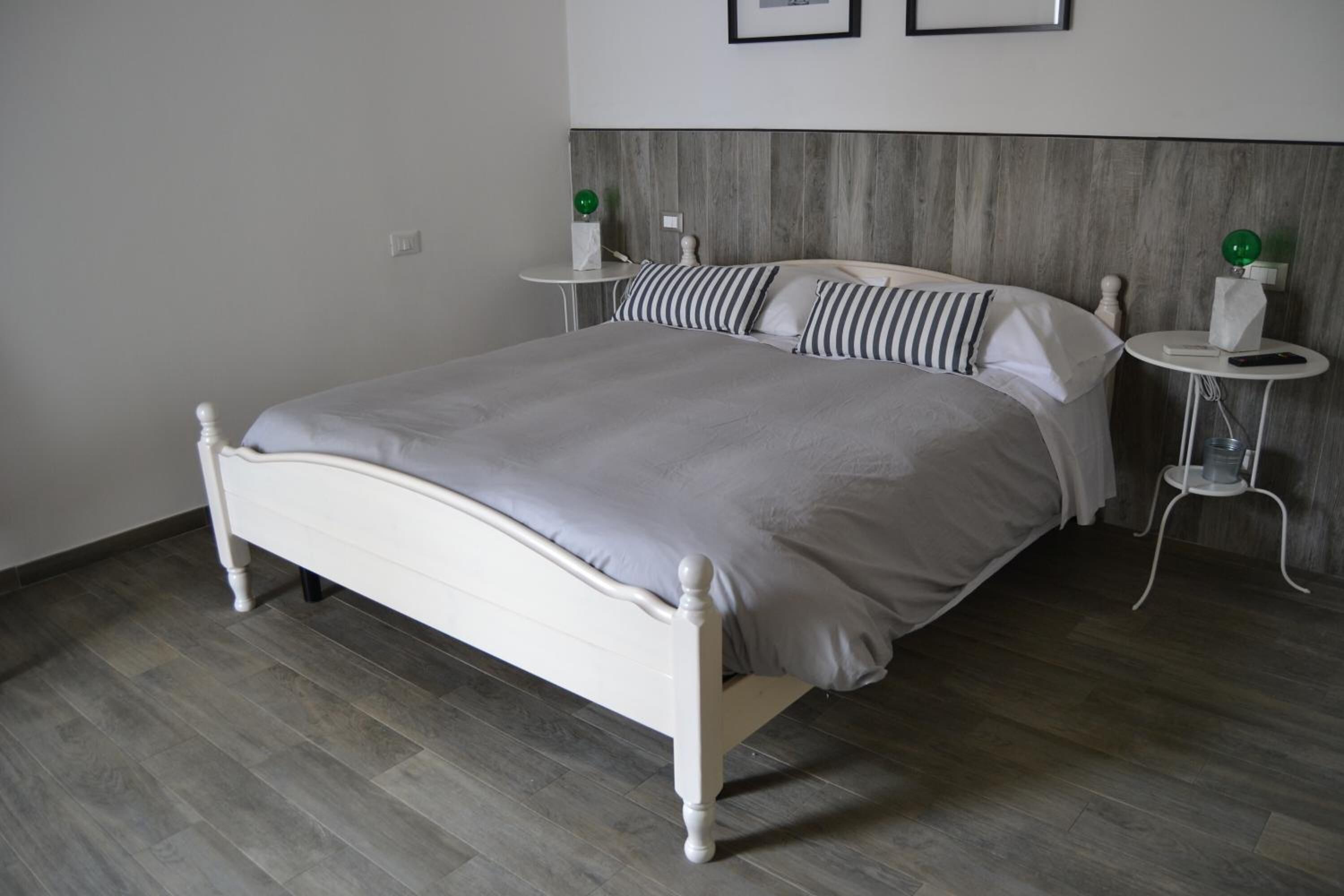 A neatly made bed with a grey bedspread, a bedside table with a green object, and a wall-mounted shelf with a white object.