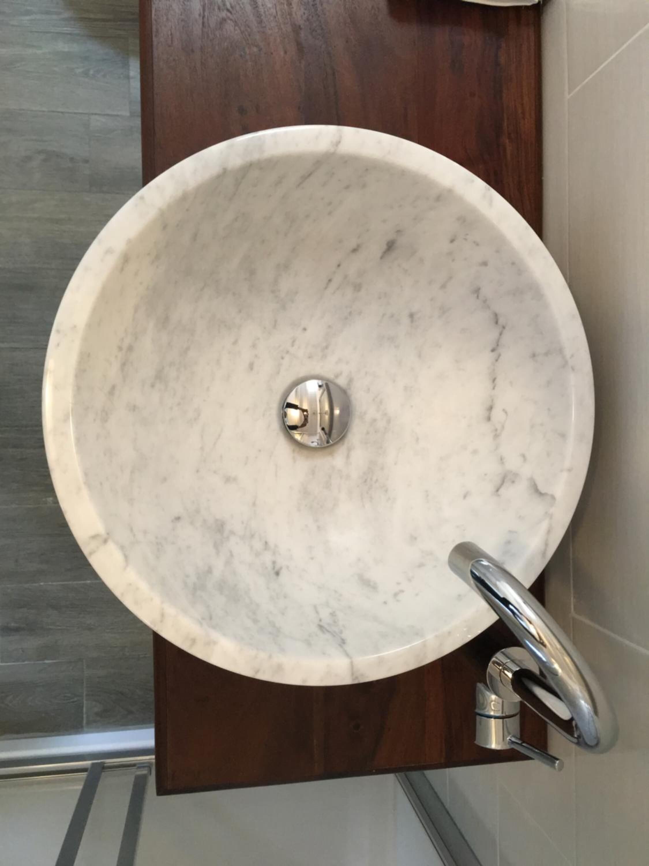 Un lavamanos redondo de mármol con un solo grifo sobre un panel de madera.