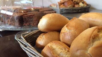 A table with a glass display case containing a slice of cake and a basket of bread rolls.
