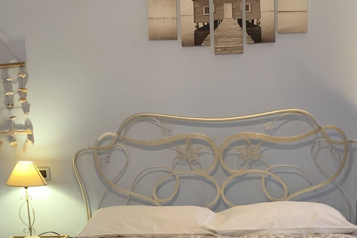Un dormitorio con cama, mesita de noche, lámpara y una obra de arte colgada en la pared.