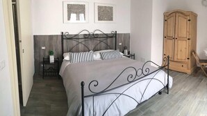 Um quarto com cama, guarda-roupa de madeira, uma mesinha e uma cadeira.
