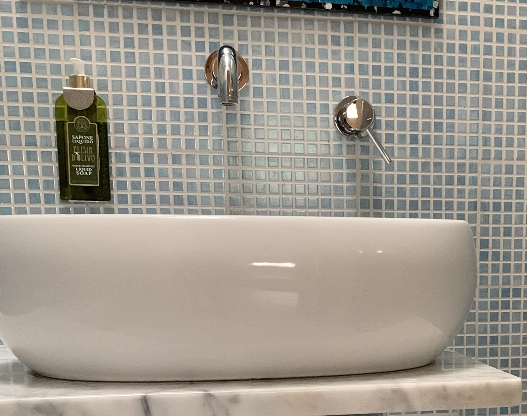 Baño con lavamanos blanco, dispensador de jabón y grifo frente a una pared de azulejos.