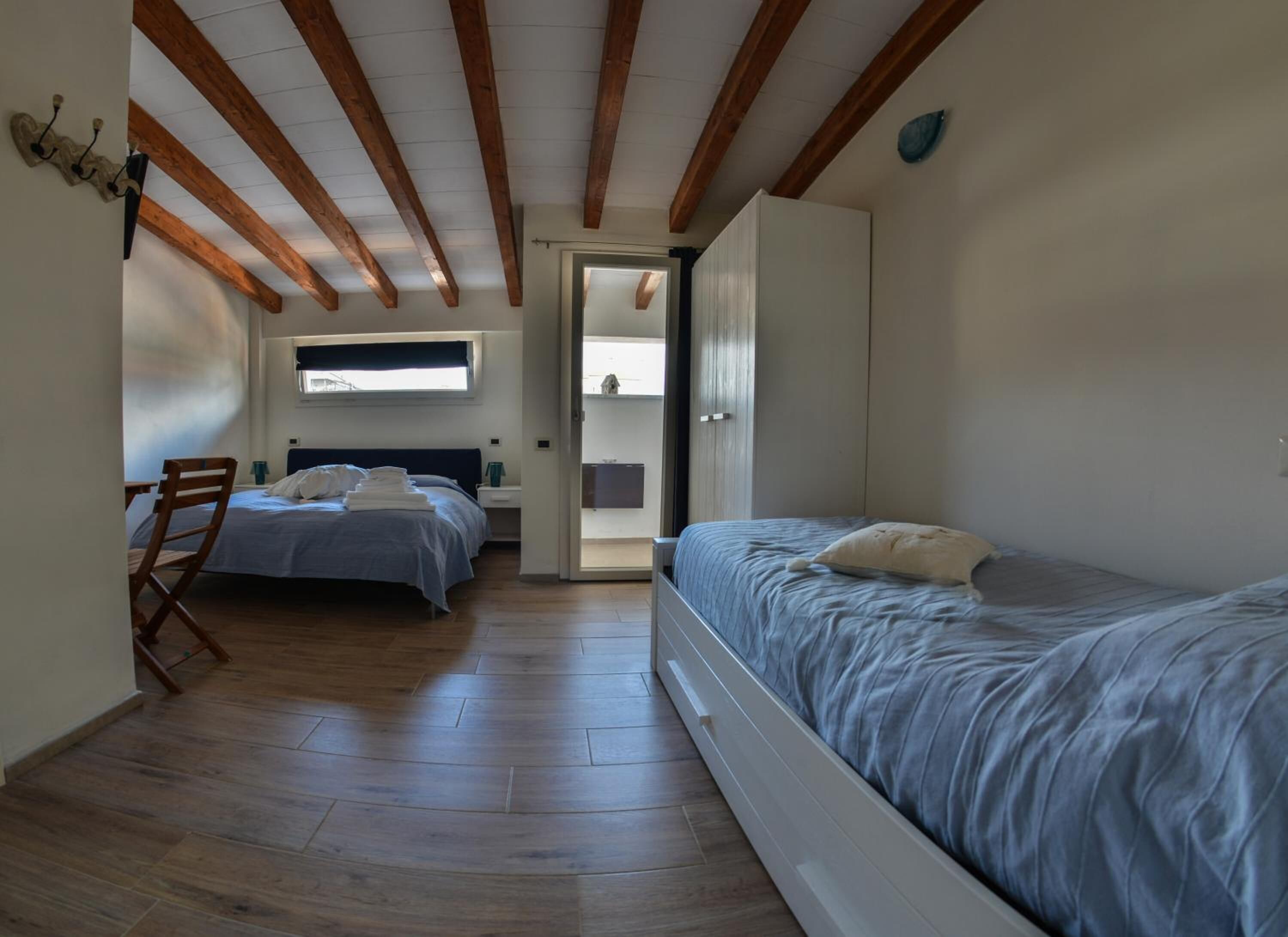 A bedroom with two beds, wooden flooring, and a sloped ceiling with exposed beams.