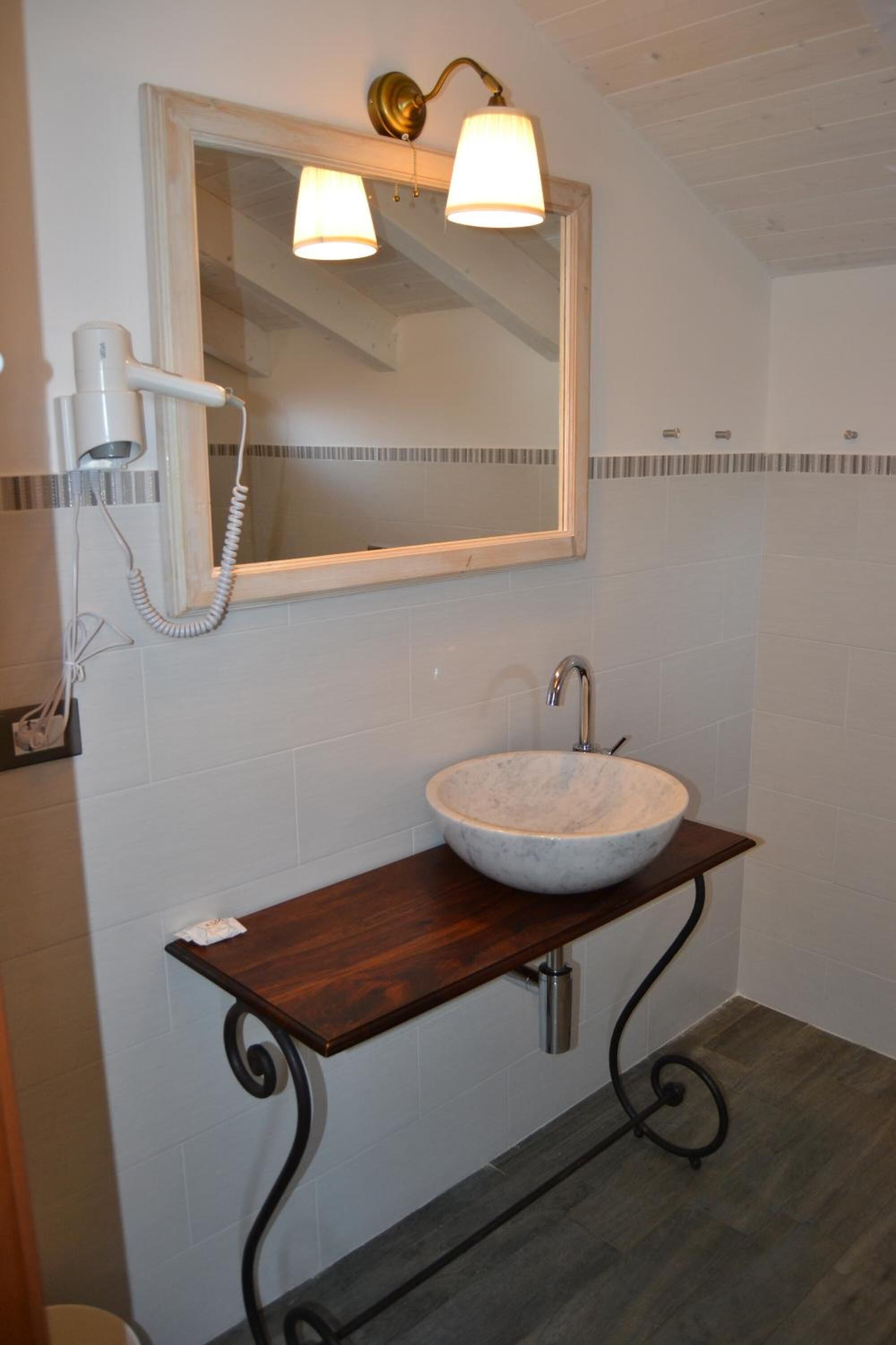A bathroom with a marble sink, a wooden vanity, a wall-mounted mirror, and a hairdryer.