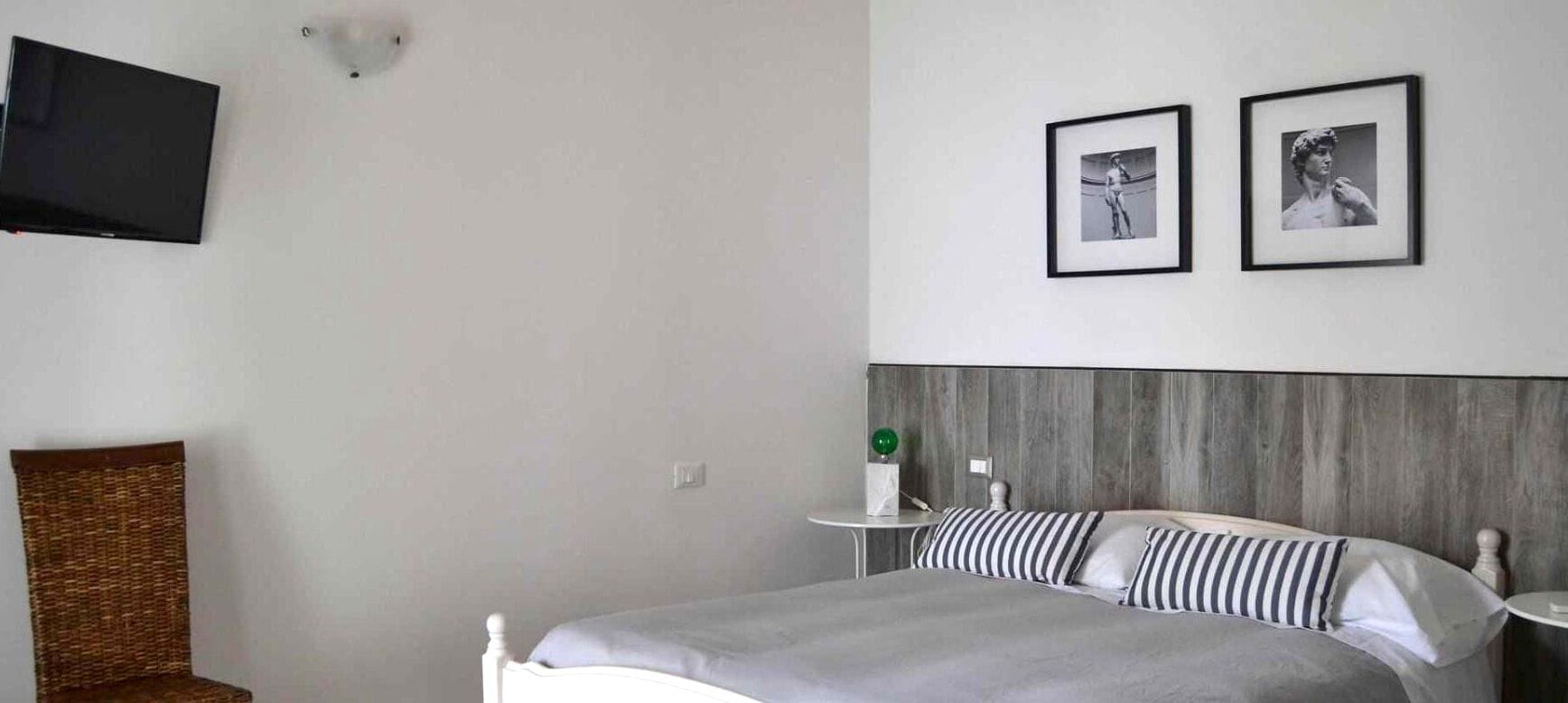 A bedroom with a bed, a chair, a TV mounted on the wall, and two framed pictures.