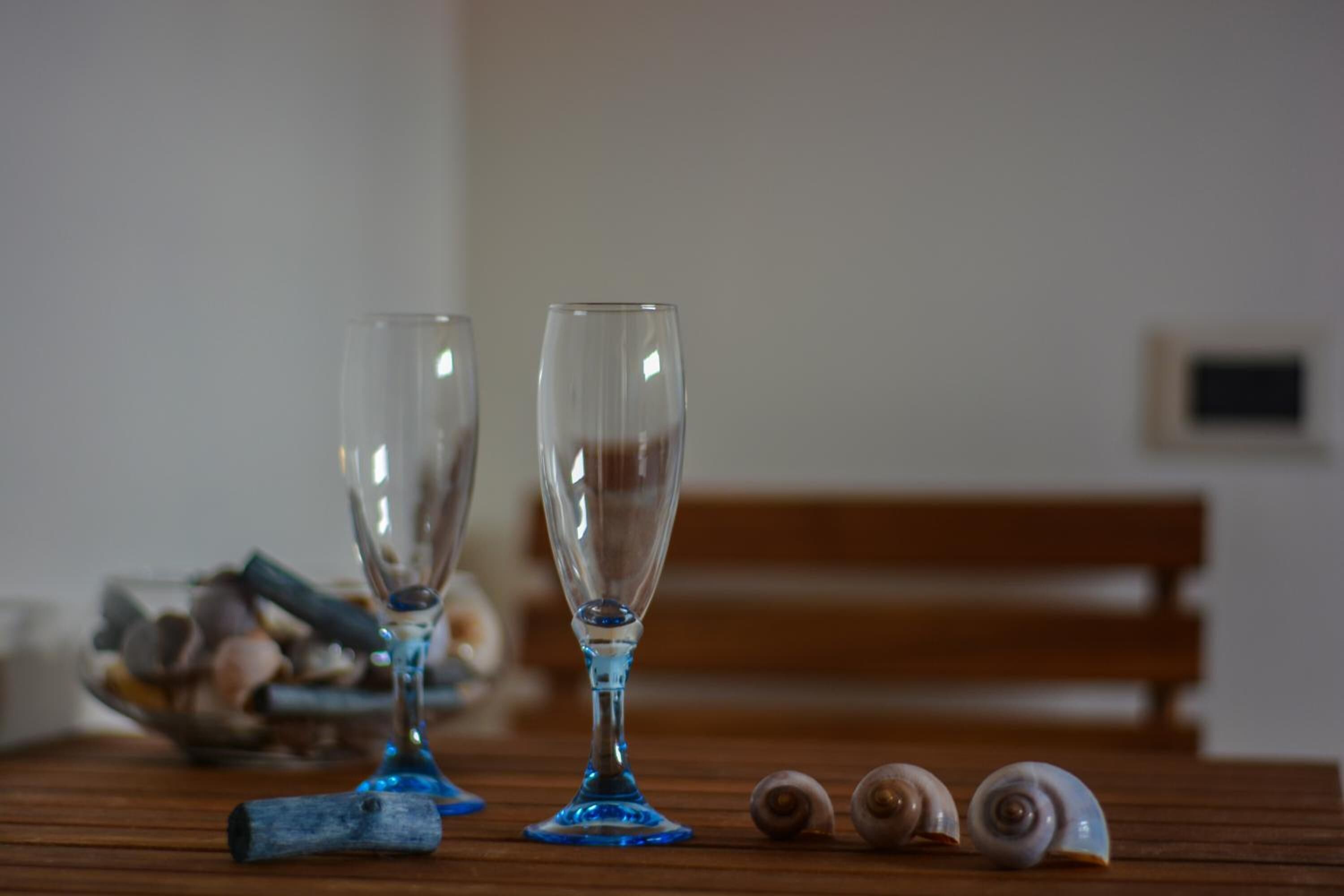 Two empty glasses on a wooden table with a bowl of seashells and a few snails.