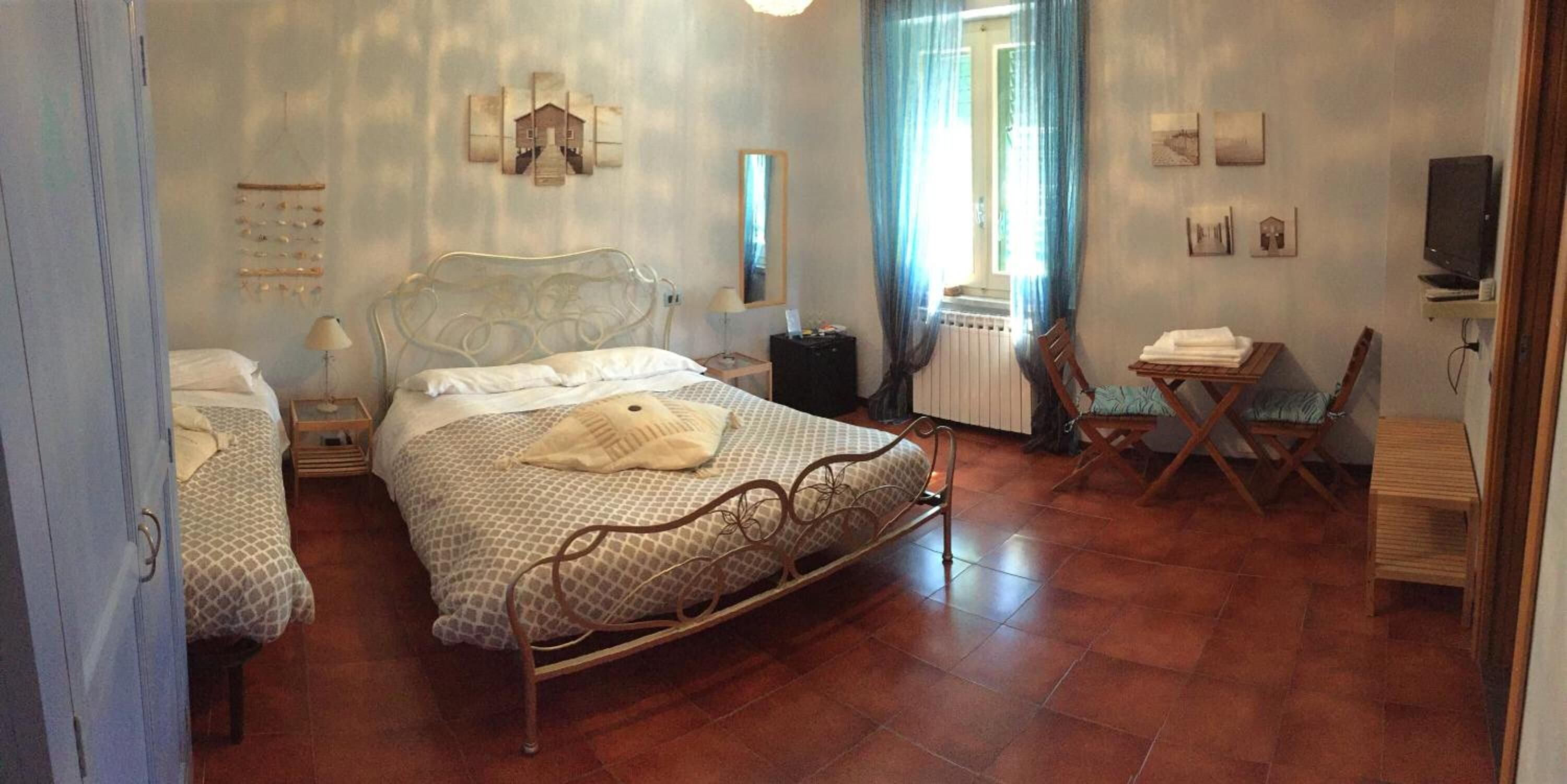 Un dormitorio con estructura de cama metálica, mesita de noche, silla, radiador y televisor.