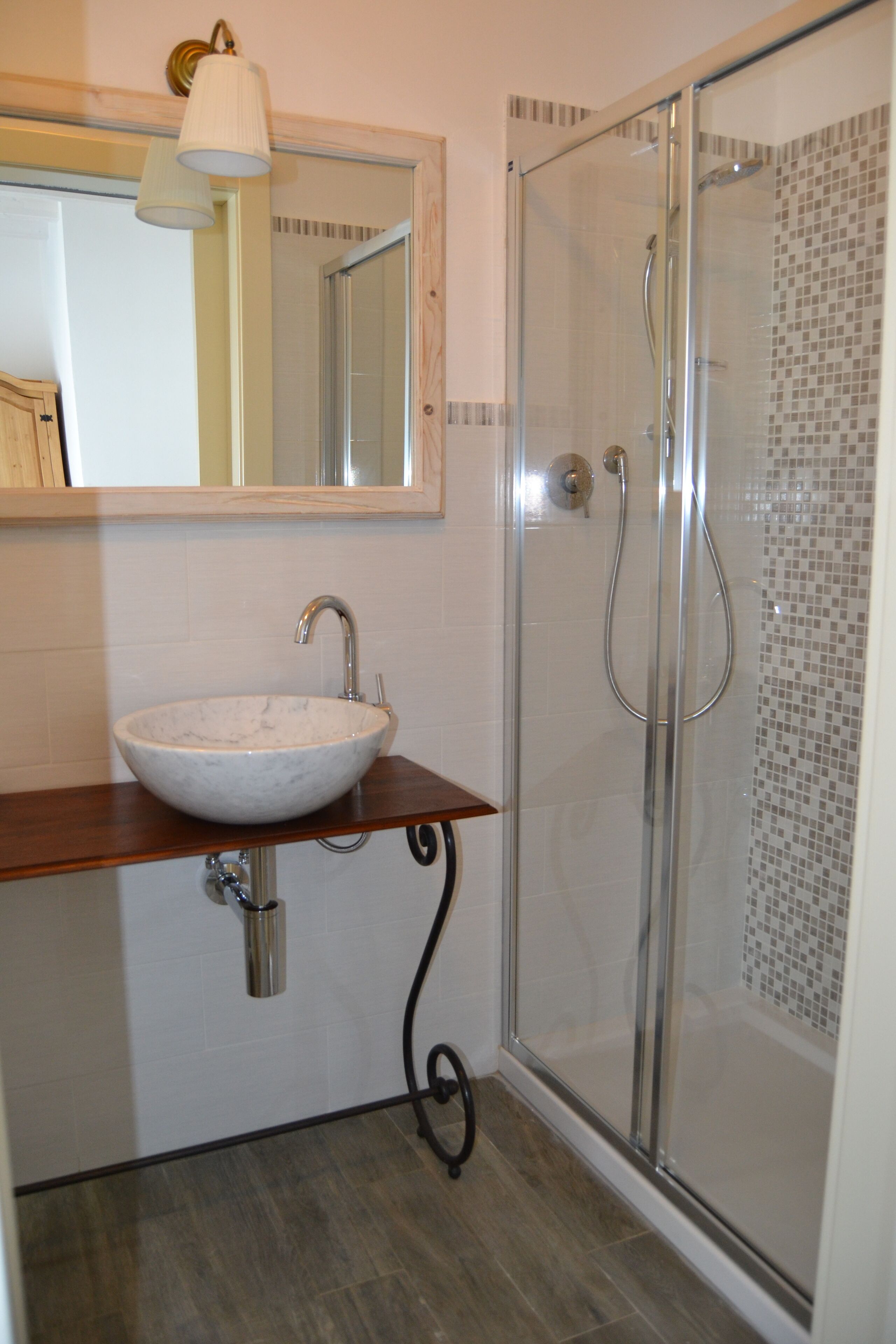 Un bagno con lavabo in marmo, cabina doccia in vetro e mobile bagno in legno.