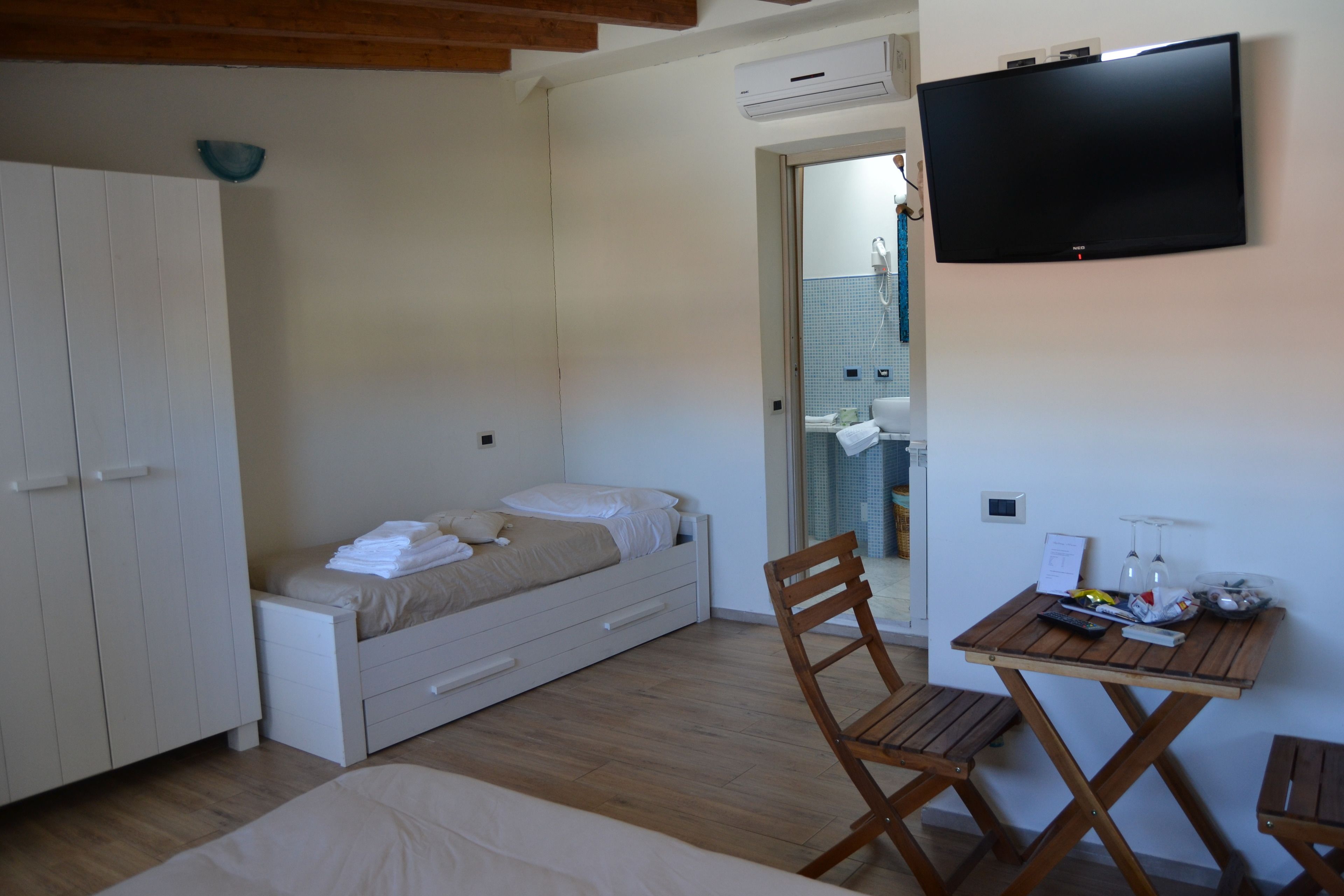 Een slaapkamer met een bed, een houten stoel, een klein tafeltje en een televisie aan de muur.