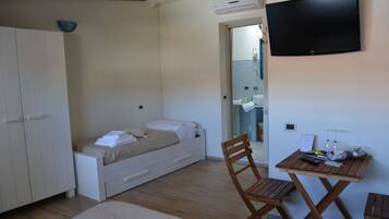 Een slaapkamer met een bed, een houten stoel, een klein tafeltje en een televisie aan de muur.