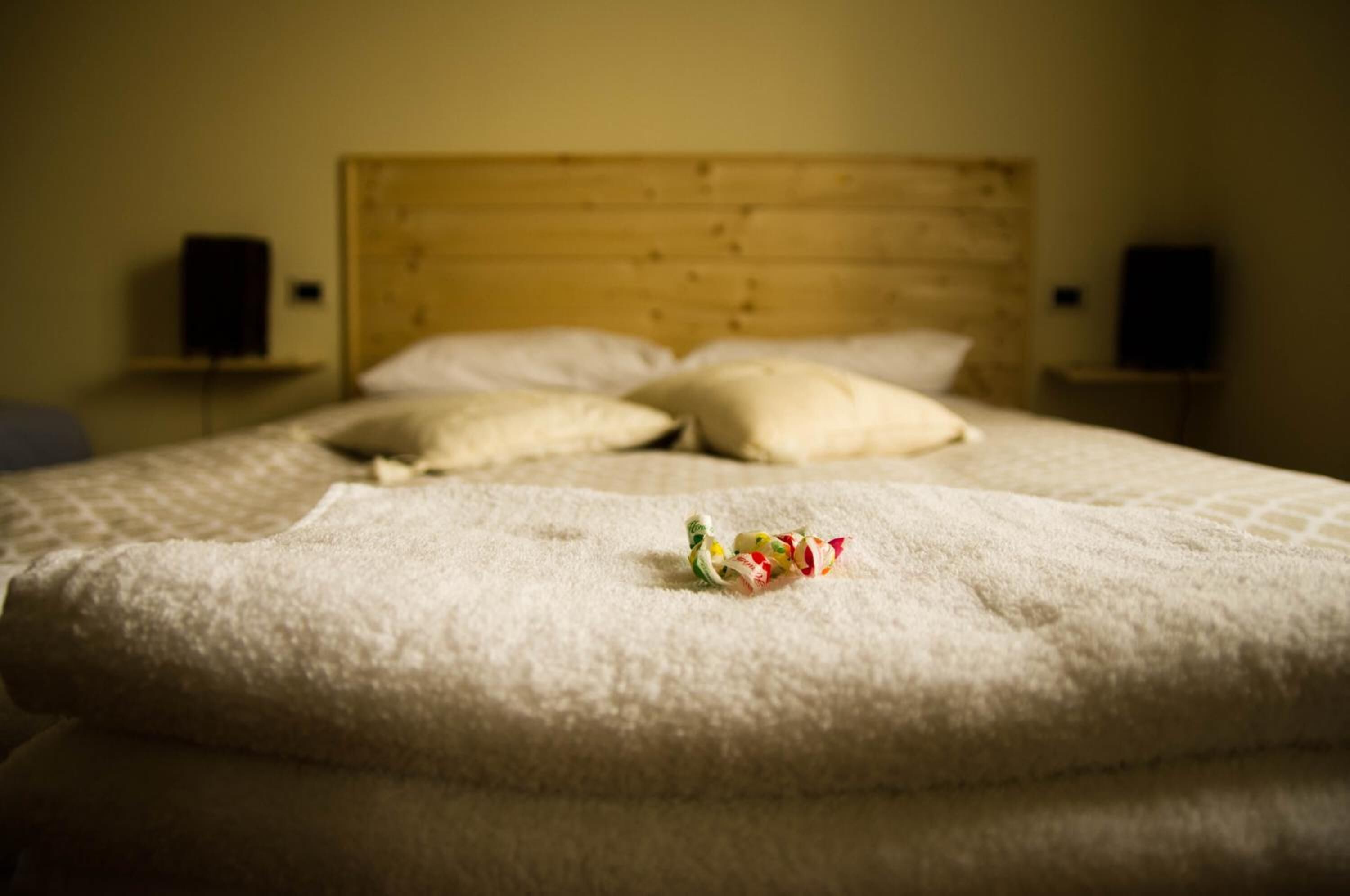A bed with a wooden headboard, white bedding, and two speakers on nightstands.
